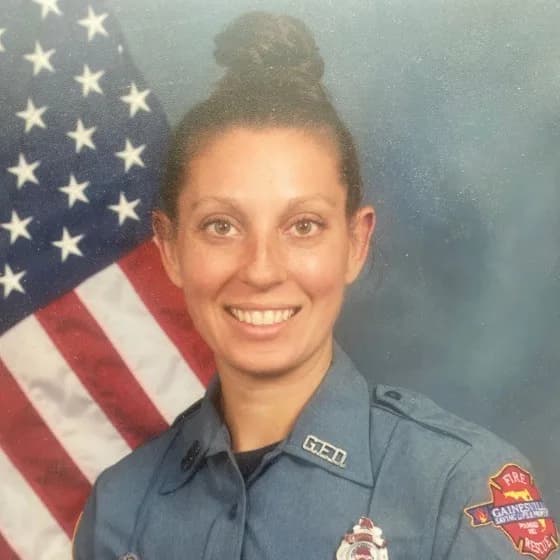 Marie Balak in a Gainesville Fire Rescue uniform in front of an American flag, smiling