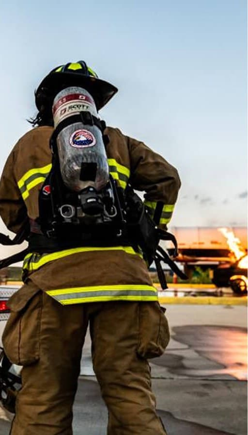 A firefighter in turnout gear and breathing apparatus at dusk.